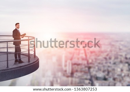 Confident businessman with planner standing on skyscraper balcony with blurred city in background. Concept of leadership. Toned image