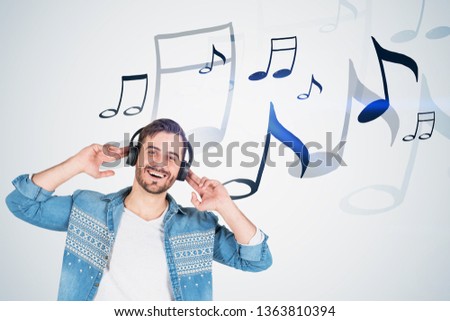 Smiling young man in headphones and casual clothes enjoying listening to music standing over white wall background with notes drawn on it. Toned image double exposure