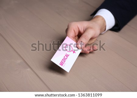 Man holding medical business card at wooden table, closeup. Women's health service