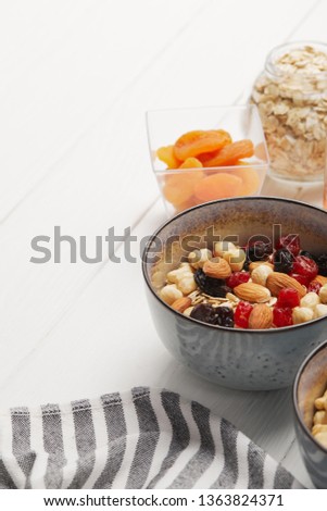 bowls with muesli, dried berries and nuts served for breakfast with dried apricots on white wooden table with copy space