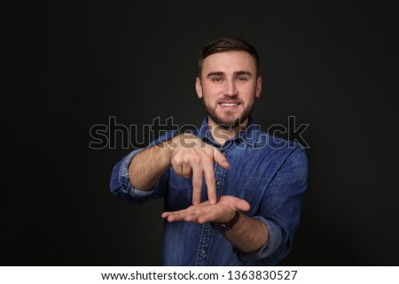 Man showing STAND gesture in sign language on black background