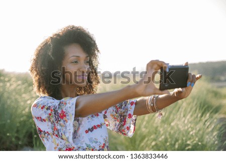 Happy young beautiful black woman using smartphone camera for taking a photo at the beach on summer or spring vacation.