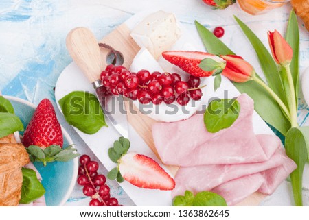 Breakfast or a dinner table with various delicacies for Easter meals. Fresh strawberries and currants with soft cheese and red spring tulips. Drinks and snacks for the holiday. Top view