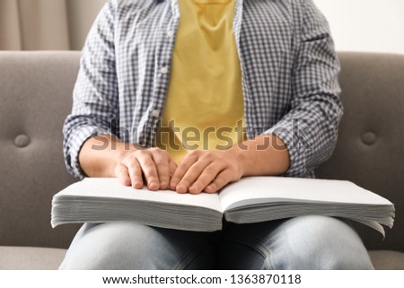 Blind man reading book written in Braille on sofa, closeup