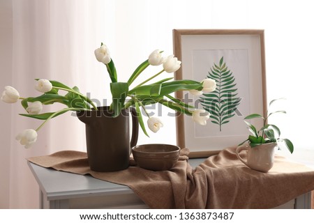 Beautiful tulip flowers with picture on table in room