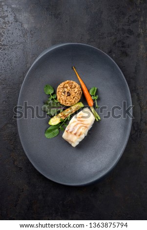 Fried Danish skrei cod fish filet with vegetable, lettuce and mushroom rice as top view on a modern design plate 