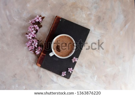 A cup of aromatic hot drink placed on a book and a column of spring flowers. Top view