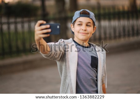 Young boy make a selfie on smartphone in the centre of the city. Cute boy in blue hat. Stylish school boy