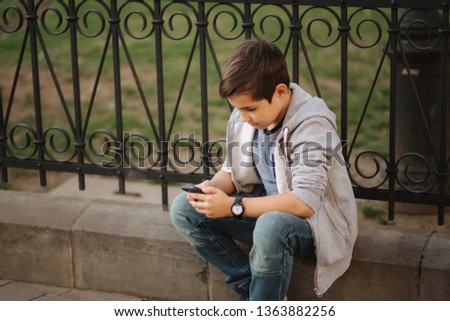 Young boy playing with smaptphone. Schoolboy using mobile phone on the street