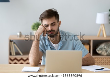 Tired bored student or employee working with laptop, doing boring routine monotonous job, looking at screen, lazy sleepy man feeling exhausted, lack motivation, distracted, sitting at workplace