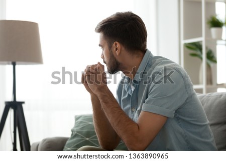 Thoughtful serious man sitting on sofa alone at home, lost in thoughts, thinking about problem solving, feeling lonely, making important decision, having psychological problem, side view Royalty-Free Stock Photo #1363890965