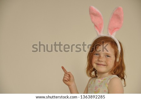 Happy child having fun on Easter egg hunt. Cute little girl with red hair wearing bunny ears holding Easter egg. Stylish kid with colorful eggs.