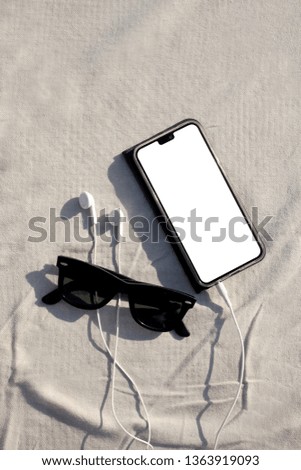 sun glasses, smartphone and earphone rest on a fabric mat with clipping path on the phone screen and copy space for your text