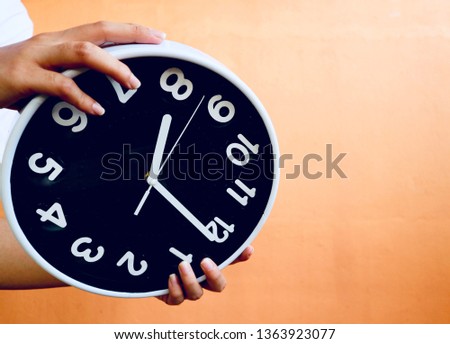 Hand hold giant clock upside down in orange background