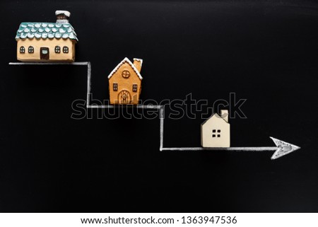 going down arrow with samller and smaller houses on blackboard background