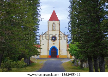 A high pine trees path frames the colorful church of Mouli. South of Ouvea, Loyalty Islands, New Caledonia.