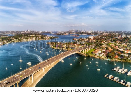 Concrete arch of Gladesville bridge over Parramatta river in Sydney Inner West with view of distant Sydney city CBD and local marina docked floating yachts.