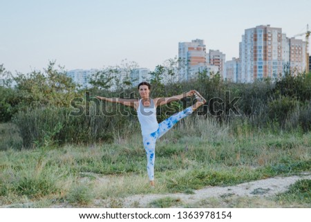 Healthy young woman doing yoga exercises on the nature in the morning on the background of the city