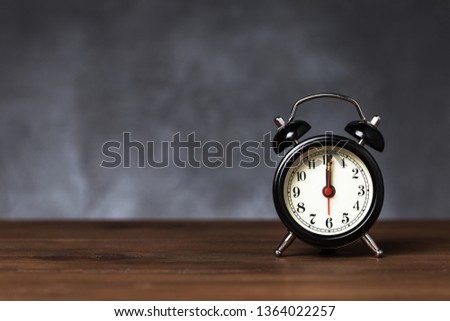 Clock hand at 12 o'clock alarm at 6 o'clock. Vintage / retro black analog alarm clock on wooden table with copy space on dark background