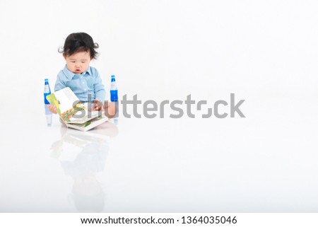 The baby is sitting on a white background and reading a picture book.