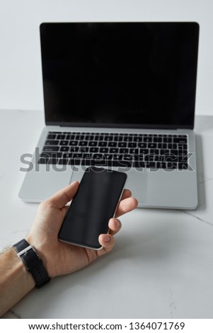 cropped view of man holding smartphone and laptop with blank screen isolated on grey