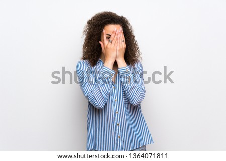 Dominican woman with striped shirt covering eyes by hands and looking through the fingers