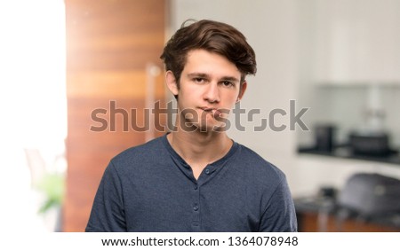 Teenager man with confuse face expression while bites lip at indoors