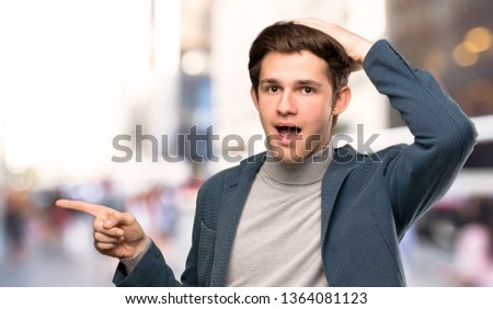 Teenager man with turtleneck surprised and pointing finger to the side at outdoors
