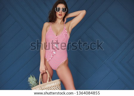 Nice outfit. Stylish beautiful young girl in bikini stands and posing in the studio.