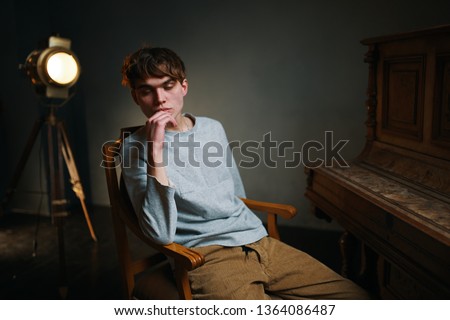 A man is sitting on a chair next to a spotlight and a piano