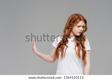 upset redhead girl showing stop sign and looking away isolated on grey with copy space