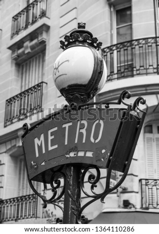 Vertical black and white image of a Metro subway entry sign with Haussmann building background in Paris France