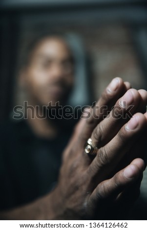 Picture of a man with his eyes closed praying. The background is blur and the focus is in the hands 