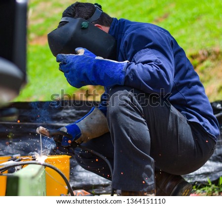 Man working welding use blue protection equipment. Green grass background.