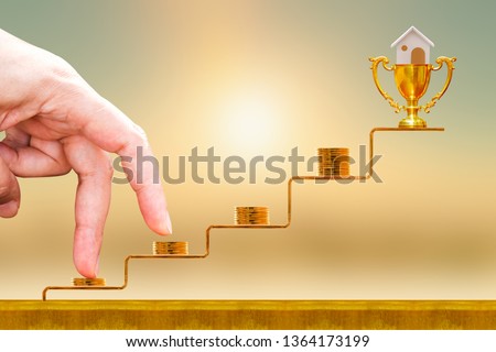 Close up of hand with climb up on a stacking five gold coin with growing on golden steps and trophy with home as destinations on sunlight background, Loan for real estate or buy the house concept.