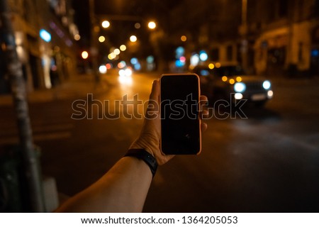 A man's hand holding a smartphone with a black screen. In the background street