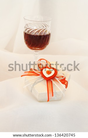 Gifts for the beloved and glass of wine. White satin background. Focus on gift.