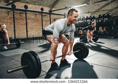 Smiling man in sportswear preparing to lift barbells during a weightlifting class in a gym Royalty-Free Stock Photo #1364211266