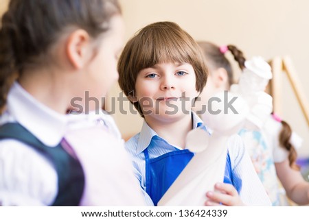 boy draws in the classroom with the other children, the children stand in a row in the table