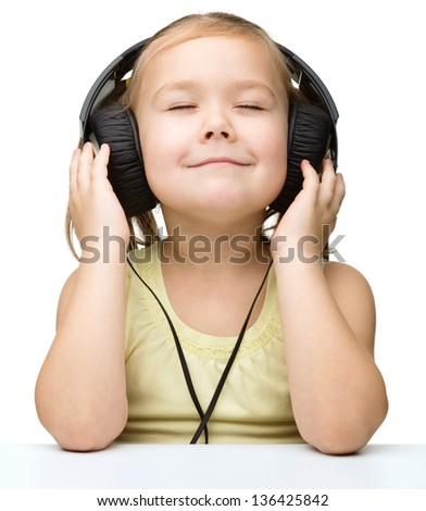 Cute little girl is enjoying music using headphones and closed her eyes, isolated over white