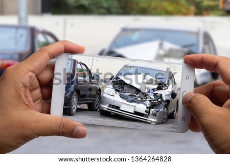 Car insurance agents take pictures of silver accident-damaged vehicles with a smartphone as a proof of insurance claim.