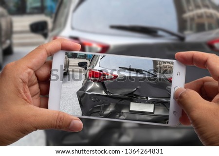 Car insurance agents take pictures of black car accident-damaged vehicles with a smartphone as a proof of insurance claim.