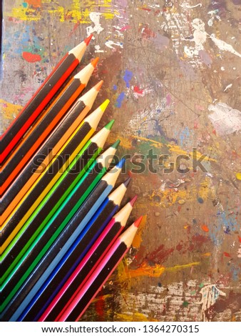 rainbow coloured pencils at an angle on a paint-splattered artists table