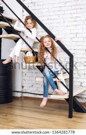 Two beautiful child girls with curly hair and fluffy rabbit animals are sitting on the stairs