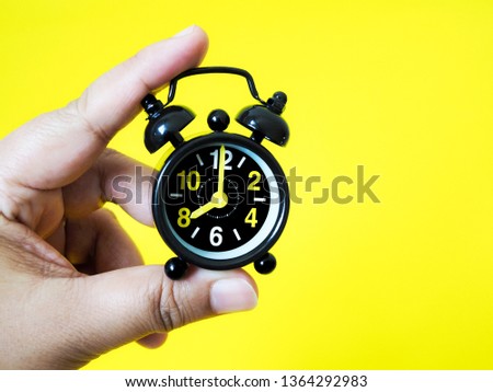 Hand holding vintage black alarm clock on yellow background with copy space. Time keeping concept