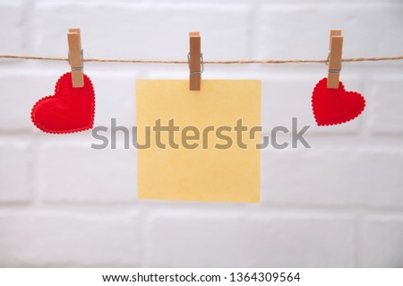 Red hearts are hung on the rope with clothespins with a sheet of paper on a white background. Congratulations on Valentine's Day.