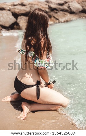 pretty young woman sitting on the seashore touching the water