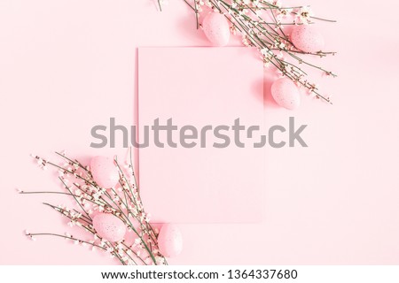 Easter composition. Easter eggs, paper blank, white flowers on pastel pink background. Flat lay, top view, copy space