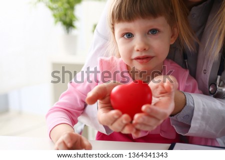 Little baby girl visiting doctor holding in hands red toy heart as life safe symbol Royalty-Free Stock Photo #1364341343