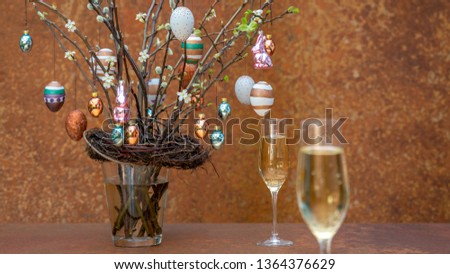 Branches with flowers and buds. Easter eggs and Easter bunnies hang on the branches. Sparkling wine bubbles in 2 champagne glasses. 